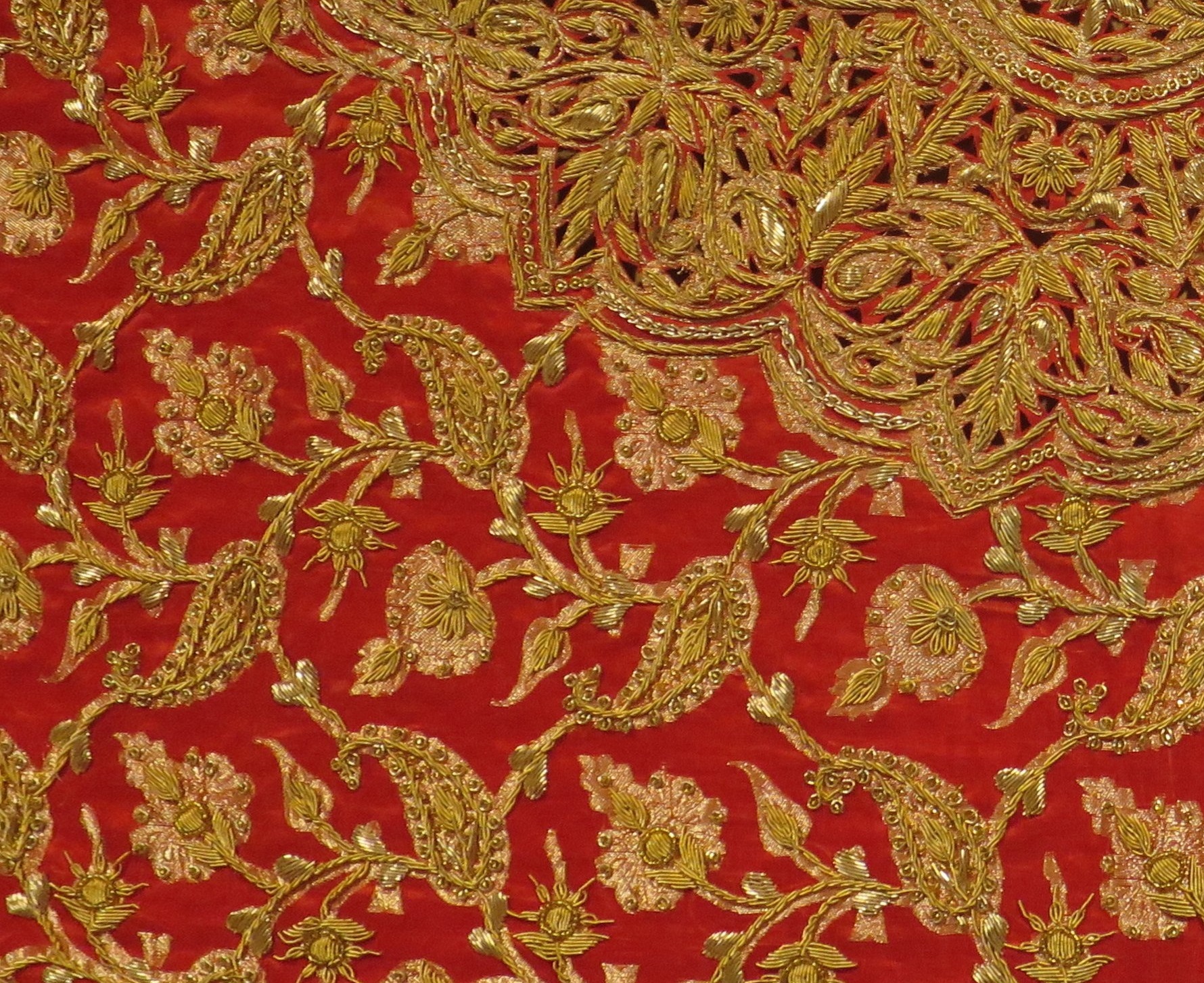 Image of red fabric with decorative gold stitches.