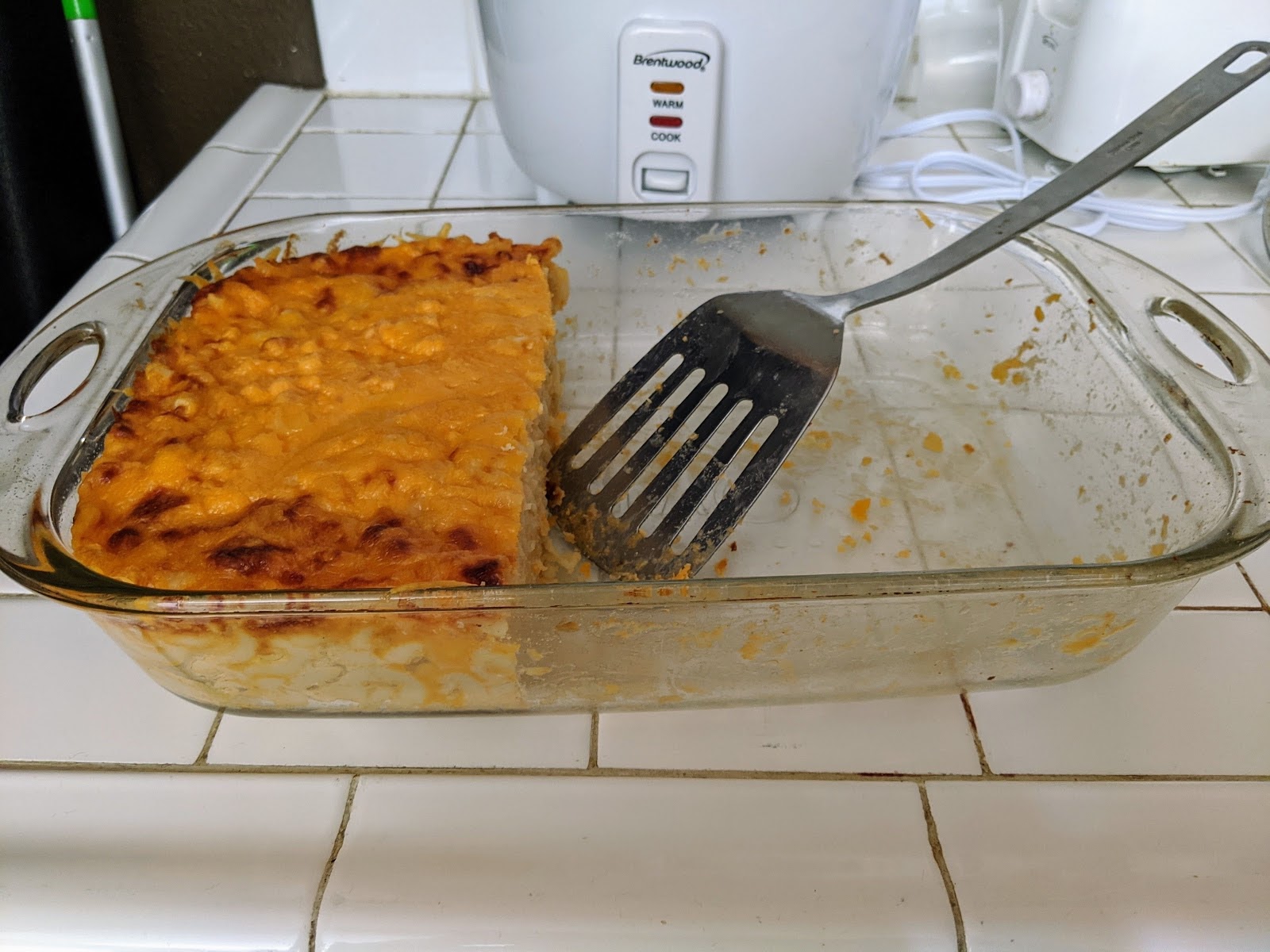 Photograph. Mac and cheese in pan with spatula. Less than 1 half remains. 