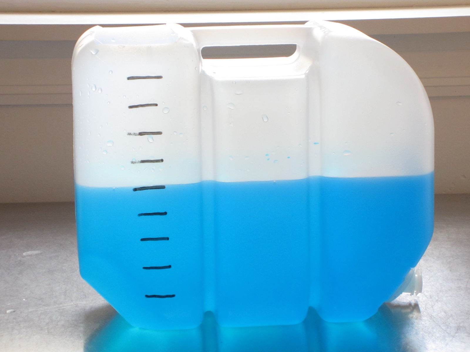 Container with hash marks measuring liters filled with liquid to the fifth hash mark.