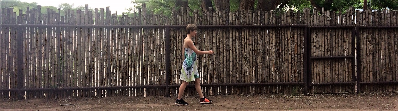 <p>An image of a woman walking along a fence. The woman is about halfway along the fence.</p>
