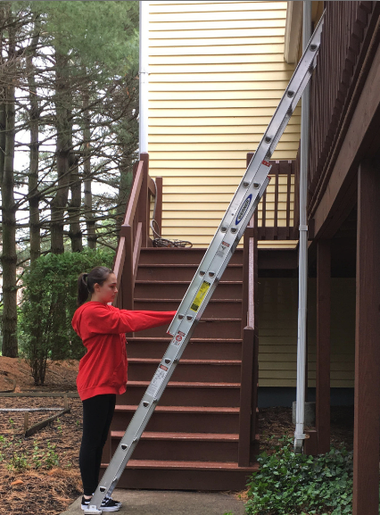 <p>Person standing with arms reached out directly in front of them touching a ladder leaning against a house.</p>
