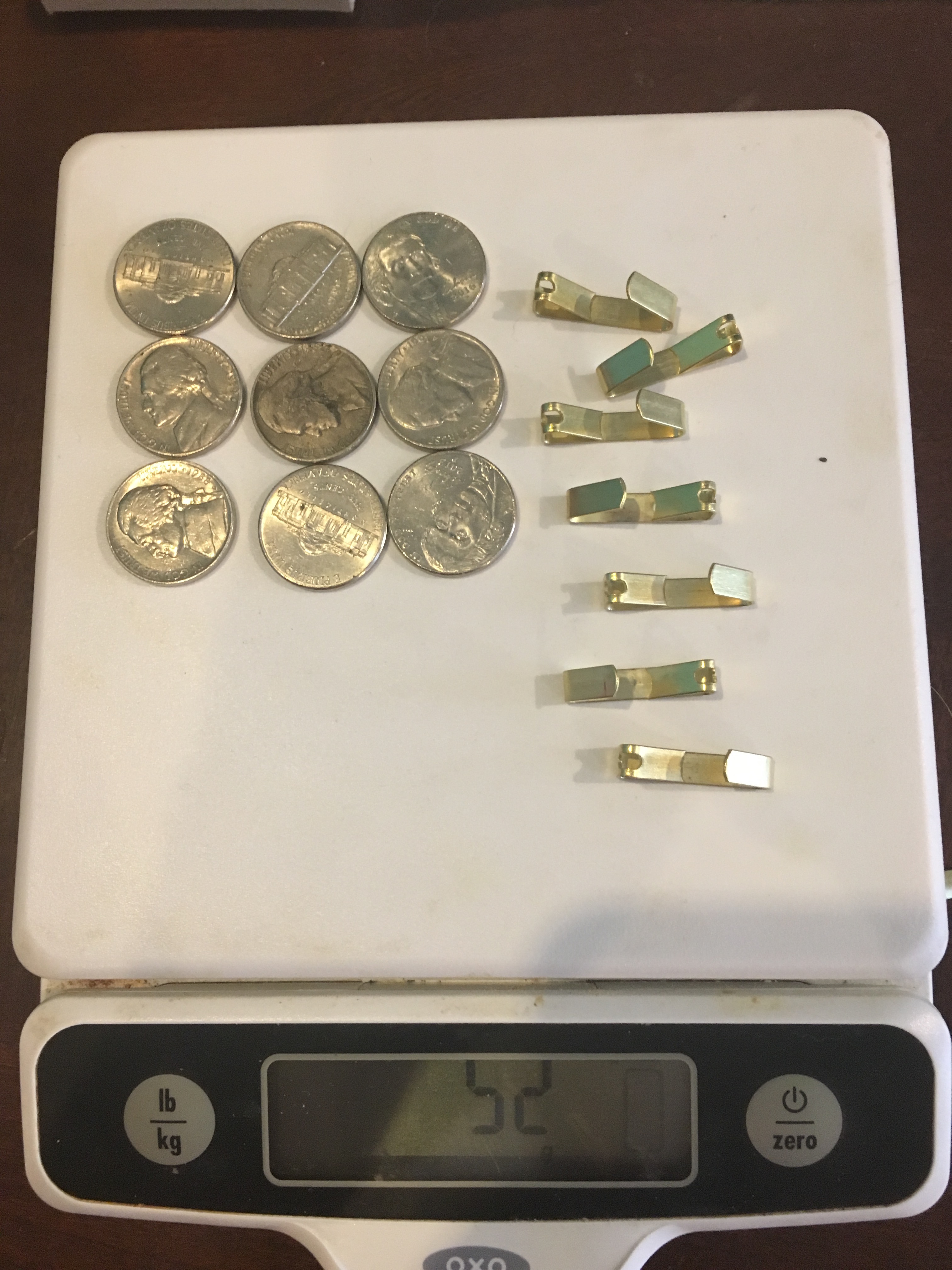 <p>Photograph, 9 nickels and 7 picture hangers on a scale, weight 52 grams.</p>

