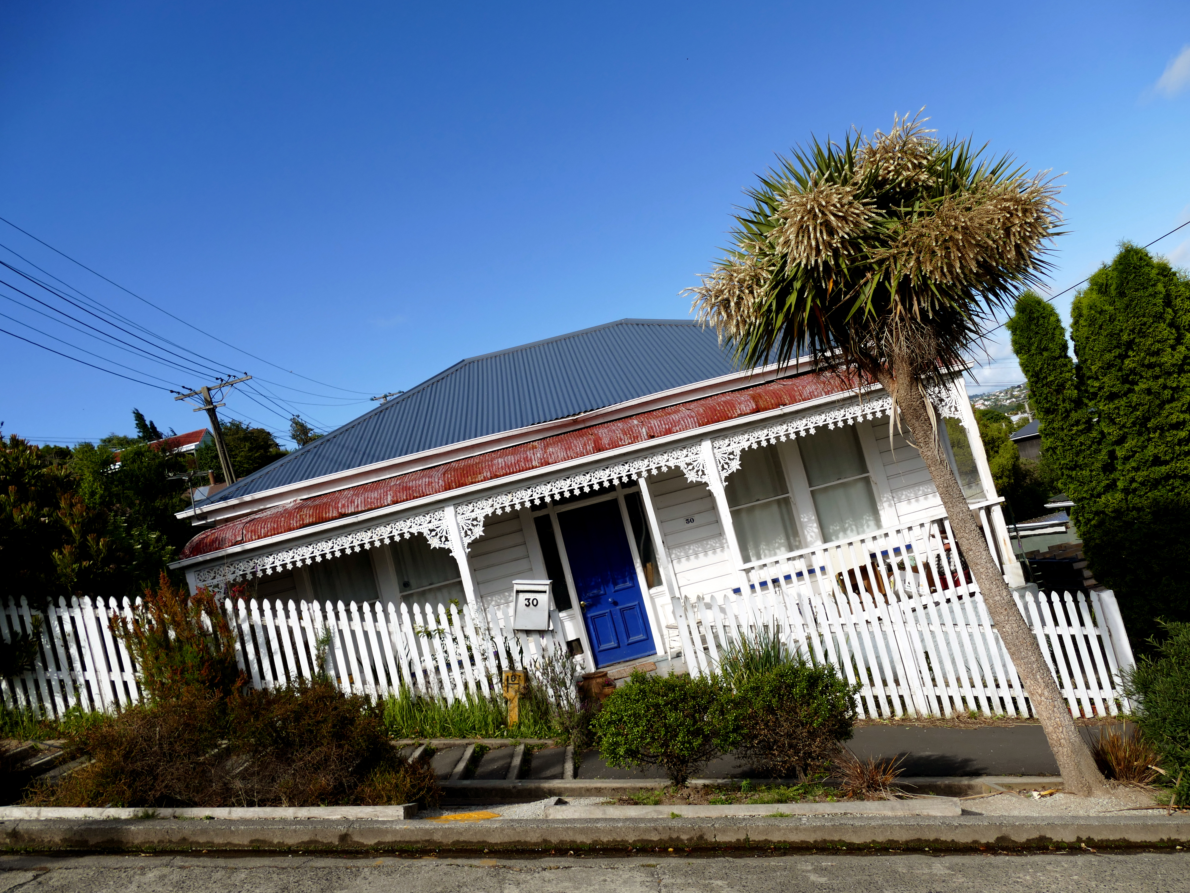 Photo of house with a fence and sidewalk in front. The house, fence, and trees seem to be tilted, not straight, but leaning to the left