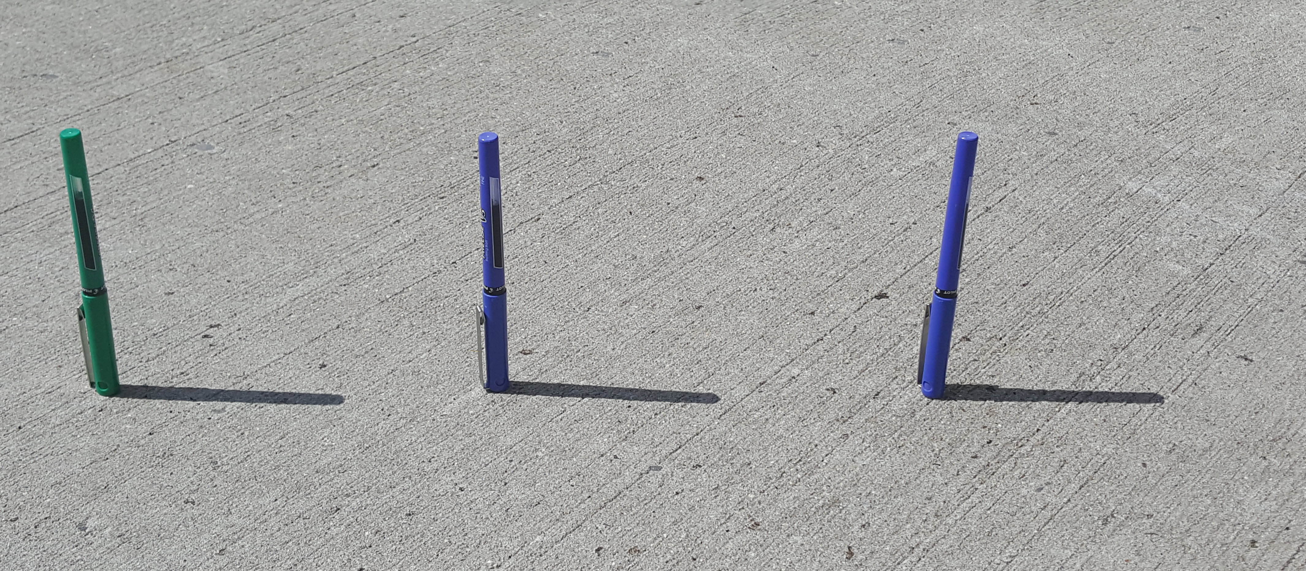 <p>Photograph of 3 pens standing upright forming shadows on the desk</p>
