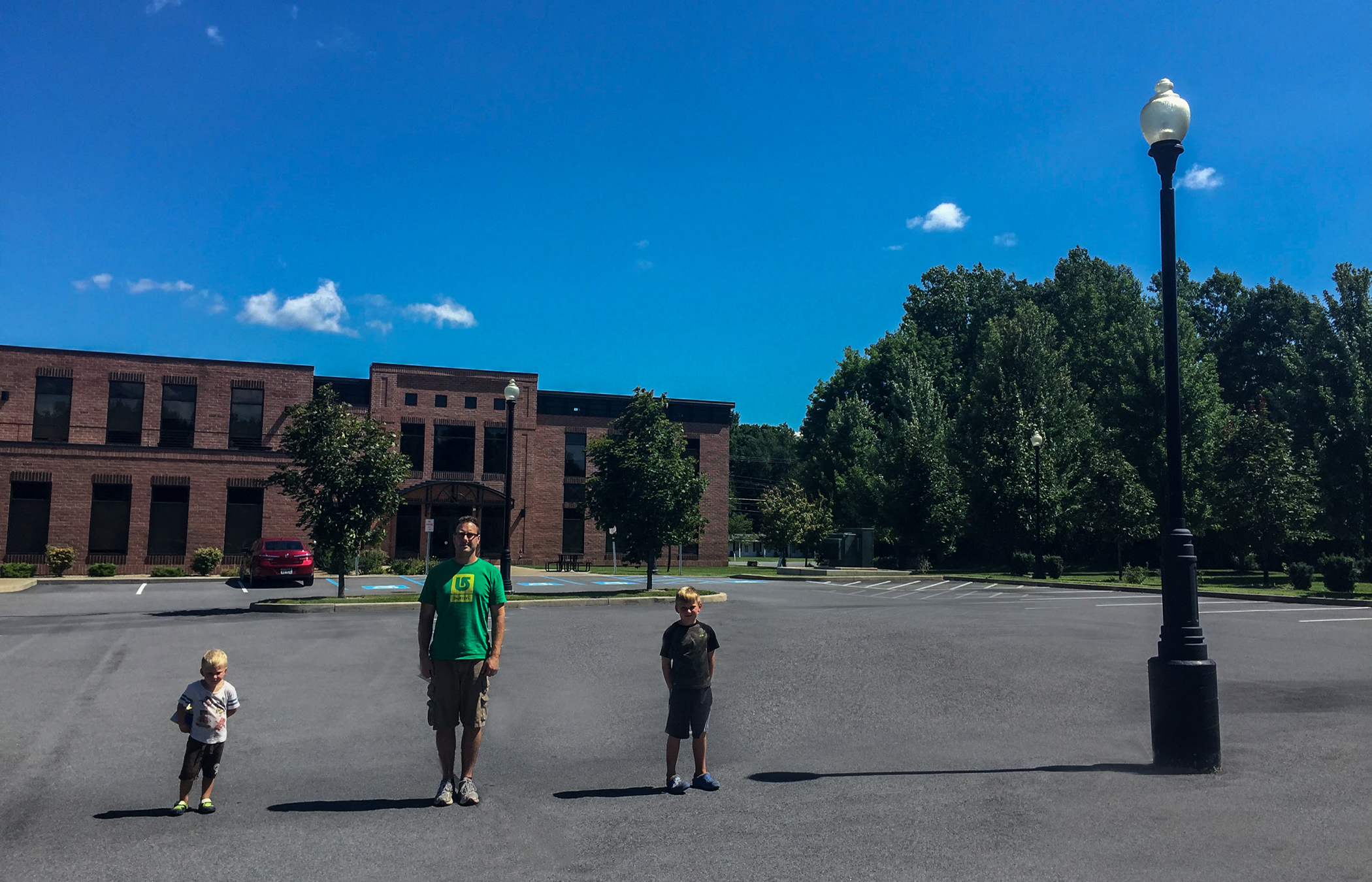 <p>Photograph of 2 boys, a man, and a lamp post, each have a shadow to their left.</p>
